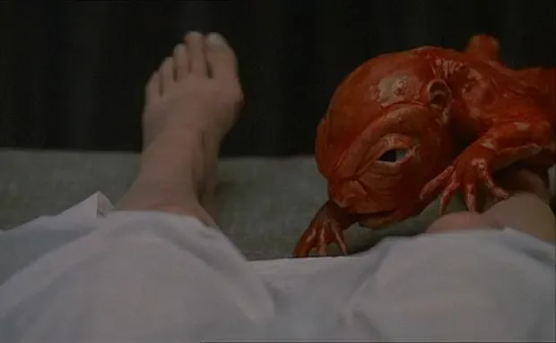 Still from To the Devil a Daughter depicting a red demonic fetus crawling across a women's legs.