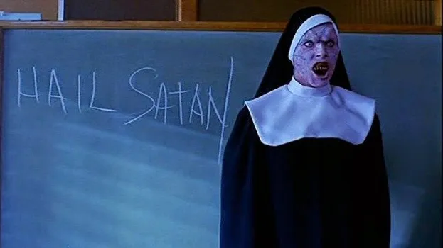 A still from the 2000 horror film The Convent depicting a scary nun in front of a chalkboard on which is written "Hail Satan!"